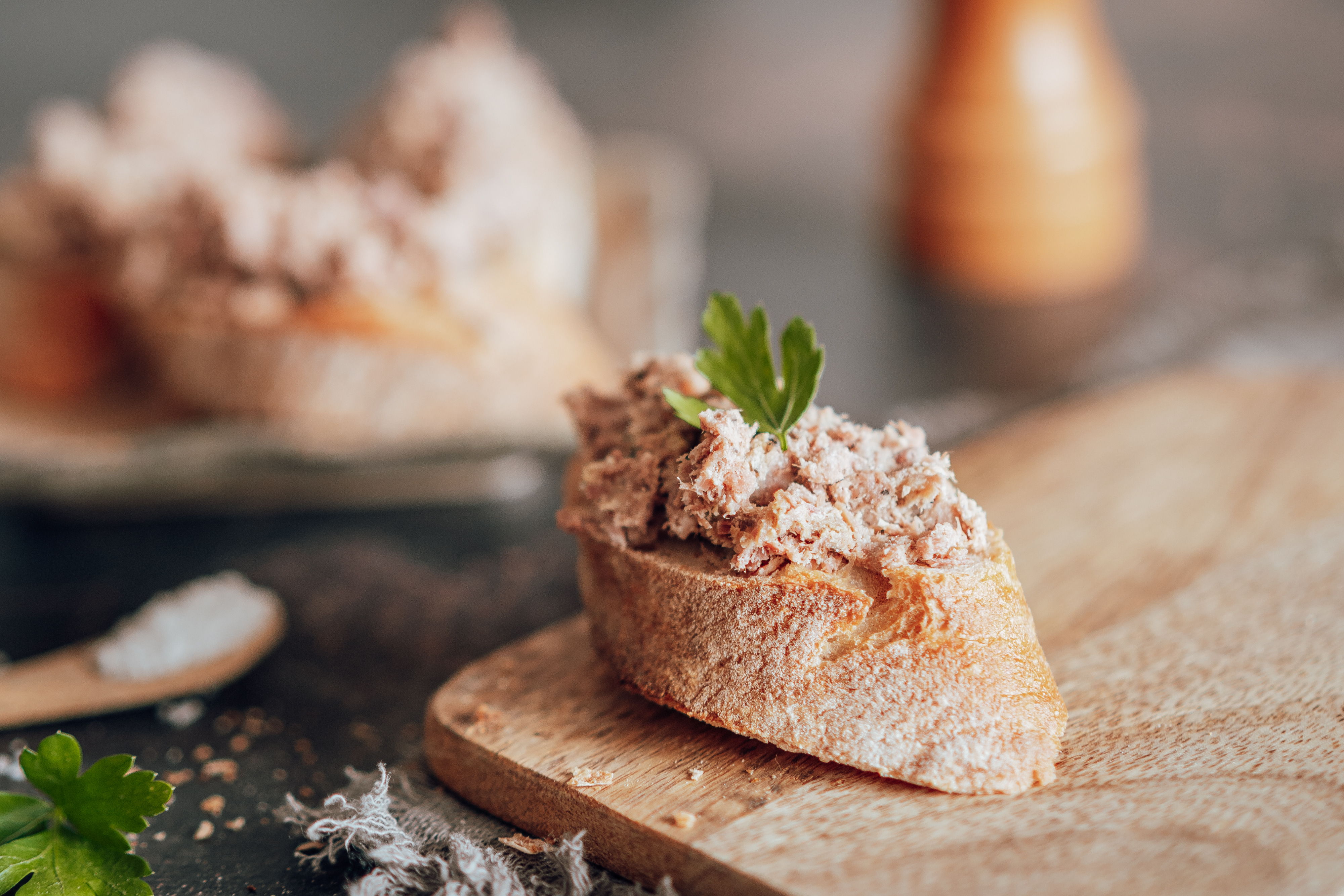 Tartine de pain frais garnie de rillettes de canard artisanales, décorée d’une feuille de persil.